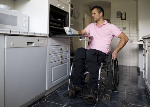 A wheelchair user takes something out of the oven in his kitchen